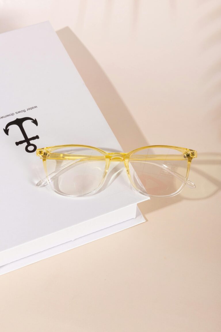 Yellow eyeglasses placed on a white book with a minimalist aesthetic.